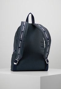 Marinblå ryggsäck med rutmönster, utrustad med justerbara remmar, en logotyp på remmen och en strukturerad tygfinish.