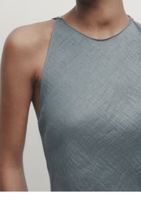 Haut sans manches gris avec un tissu texturé et froissé, présentant un col haut et un design minimaliste. Gros plan sur la section supérieure du vêtement.