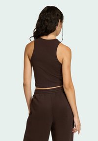 Hnedý rebrovaný krátky top bez rukávov. Zadná časť má zaoblený výstrih a priliehavý strih. Kombinovaný so zodpovedajúcimi nohavicami.
