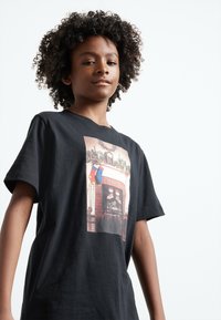 Black cotton t-shirt featuring a graphic print of a holiday scene with stockings and a fireplace. Short sleeves and a relaxed fit.