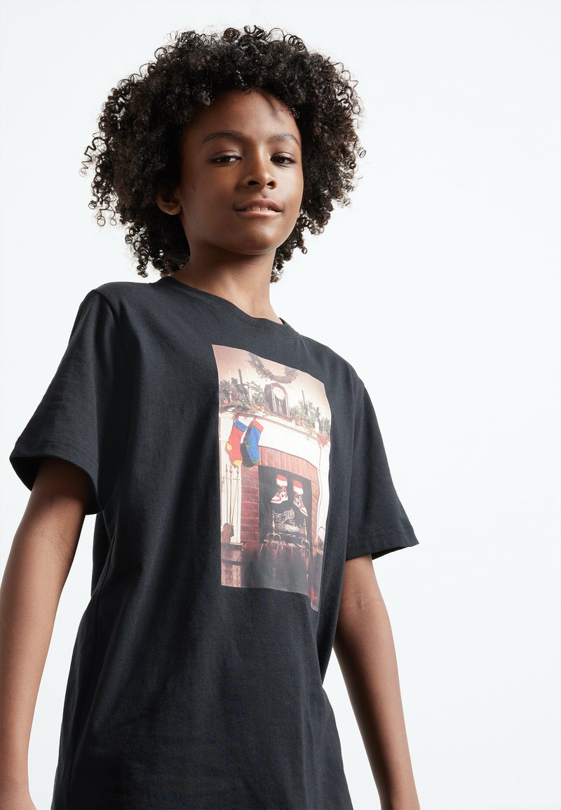 Black cotton t-shirt featuring a graphic print of a holiday scene with stockings and a fireplace. Short sleeves and a relaxed fit.