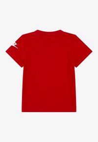 Röd bomulls-t-shirt med korta ärmar, en klassisk rund halsringning och en vit logga på vänster ärm. Slät textur, minimalistisk design.