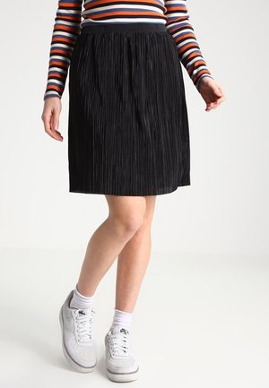 Persona que lleva una falda negra plisada, zapatillas blancas Nike con calcetines, y una camiseta de manga larga a rayas en naranja, azul marino, blanco y burdeos.