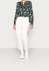 Blusa nera con stampa di foglie verdi, presenta un collo a V e maniche lunghe, abbinata a pantaloni bianchi a vita alta e stivali bianchi chunky.
