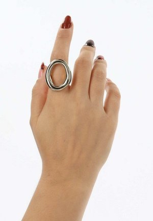 Anello in metallo con un design intrecciato e liscio. Finitura in argento lucido, forma ovale, indossato su una mano con unghie corte e manicure multicolore.