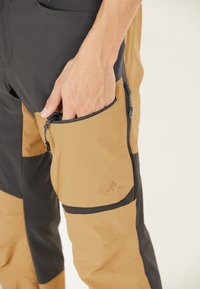 Zwarte en bruine outdoorbroeken met een ritszak. Gemaakt van lichtgewicht stof, met contrasterende kleuren en een embleem op de zak.