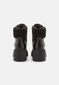 Bottines noires en cuir avec un revers en fausse fourrure noire duveteuse, semelle épaisse et fermetures éclair sur le côté. Dessus texturé et détails en finition lisse.