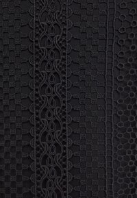 Černá tkanina s krajkovými částmi a složitými vzory, včetně kostkovaného designu a vlnících se motivů s texturovaným povrchem.