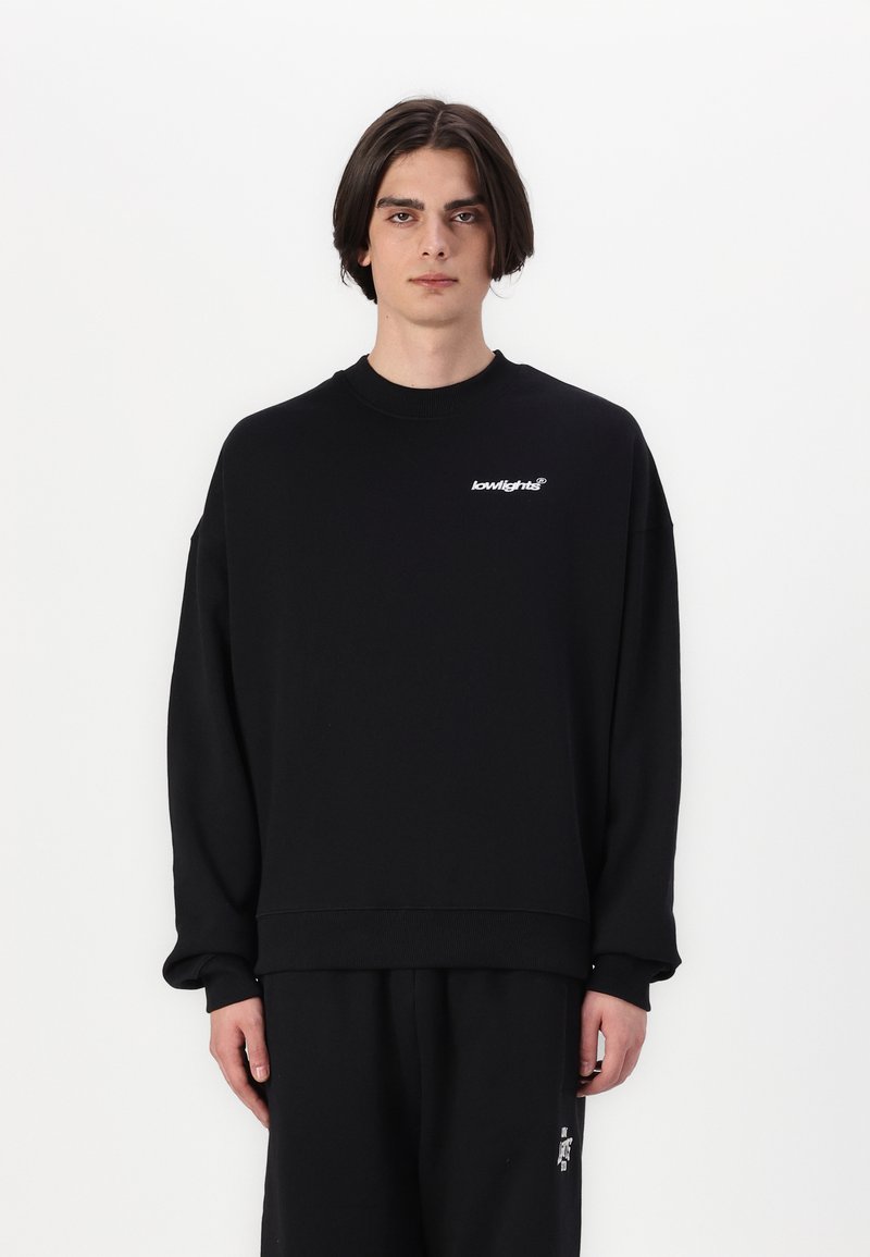 Sort sweatshirt med ribbet halsudskæring, drop skuldre og logo detalje på brystet. Blød tekstur, oversized design. Standard pasform.