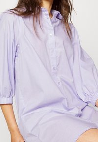 Levandulová košile s krátkými nafouklými rukávy a volným střihem, vyrobená z lehkého materiálu, s hladkým povrchem.