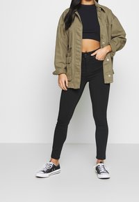 Olivgrön oversized jacka, svart crop top, svarta skinny jeans och svarta sneakers med vita sulor. Avslappnad streetwear-look.