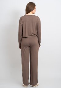Bruine cropped top met lange mouwen, gecombineerd met bijpassende wijde broek, beide gemaakt van zacht, glad materiaal en met een relaxte pasvorm.
