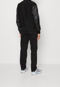 Czarna kurtka bomberka z skórzanymi rękawami, czarne spodnie oraz wielokolorowe trampki. Stylizacja charakteryzuje się minimalistyczną estetyką i smukłym designem.