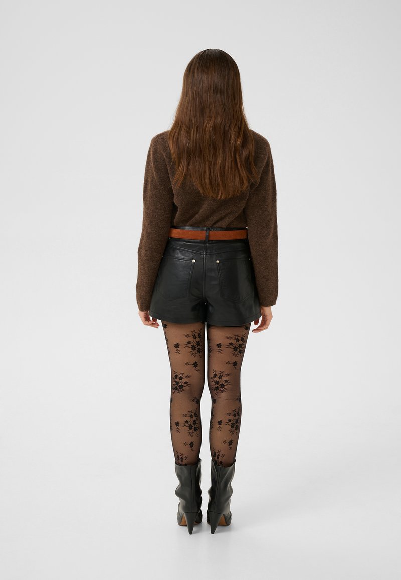 Brown textured sweater, black leather shorts, floral black tights, and black pointed-heel boots. Brown belt accentuates the waist.