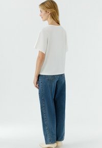 Witte top met korte mouwen gecombineerd met losse blauwe spijkerbroek, met een rechte snit en minimalistisch ontwerp, met een eenvoudig achteraanzicht.