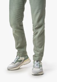 Sneaker aus einer Mischung aus grauem und grünem Mesh und Wildleder, mit weißen Schnürsenkeln und einer strukturierten Sohle. Kombiniert mit leicht grünen, schlanken Hosen.