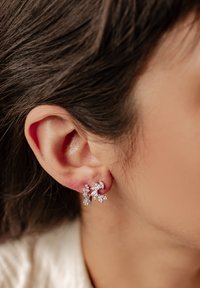 Pendientes de plata con diseños florales y m�últiples piedras preciosas transparentes. Los pendientes están colocados en la oreja, mostrando sus intrincados detalles.