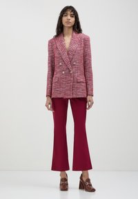 Blazer doppiopetto in tweed rosso e rosa con bottoni metallici, abbinato a pantaloni a campana bordeaux attillati e mocassini con tacco marroni.