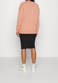 Felpa rosa con maniche lunghe, abbinata a una gonna midi nera. Le sneakers alta bianche con dettagli completano l'outfit.