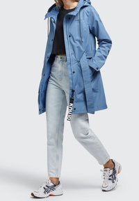 Ljusblå vattentät jacka med huva, justerbara dragsnören och tryckknappar; har sidofickor och ett texturerat midjeband.