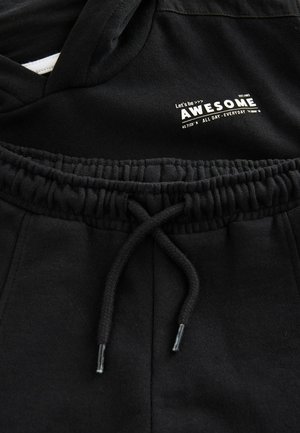Musta huppari, jossa on kiristysnauha ja valkoisella seripainatuksella teksti "AWESOME" sekä lisätekstiä. Pehmeä kangas.