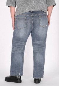 Jeansi din denim cu o nuanță albastră estompată, având o croială relaxată, buzunare la spate și detalii uzate aproape de tivuri. Asortați cu cizme negre cu talpă înaltă.