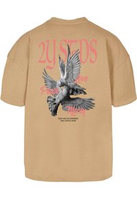 Bežinė oversized marškinėlių su juodai baltu grafiką, vaizduojančia dvi balandžius su išskleistomis sparnais. Rožinėmis spalvomis užrašytos frazės apie taiką.