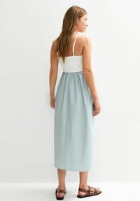 Long dress with a white fitted bodice and a light blue striped skirt. Features thin straps and a gathered waist. Worn with brown sandals.