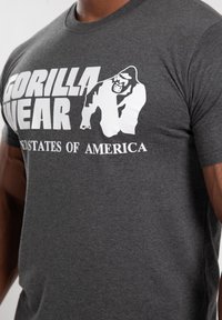 Graues T-Shirt aus Baumwolle mit weißem Druck des Markennamens "GORILLA WEAR" und einer Gorillagrafik, begleitet von "VEREINTE STAATEN VON AMERIKA."