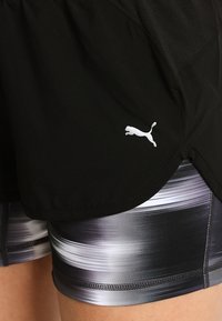 Pantalones cortos deportivos negros con un panel de malla, con un logo blanco. Debajo, pantalones cortos ajustados con un patrón de degradado gris con líneas horizontales.