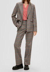 Grå rutiga kostym med orange detaljer, bestående av en skräddarsydd kavaj och raka byxor, parat med en rosa V-ringad skjorta och svarta skor.