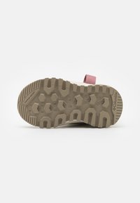 Suela de goma de color beige claro con un patrón de agarre texturizado. Diseño flexible con una correa rosa para un ajuste seguro. Adecuado para uso en exteriores.