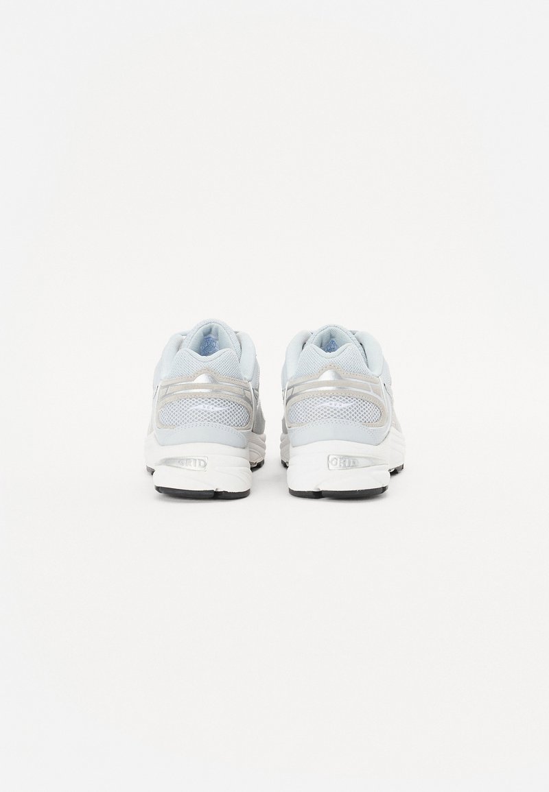 Weiße und hellgraue Sportschuhe mit einem Obermaterial aus Mesh, gepolstertem Kragen und reflektierenden Akzenten. Schwarze Gummisohle für Halt.
