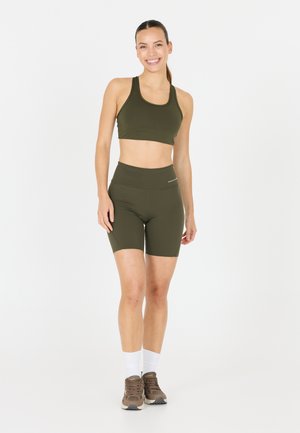 Olivgrön sport-bh och högmidjade shorts-set, tillverkat av elastisk tyg, med en slät yta och minimal branding. Bärs med beige träningsskor.
