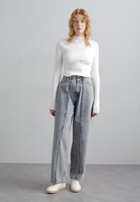 Hvid ribbet langærmet top parret med højtaljede, løstsiddende grå jeans med let slid. Hvide sneakers fuldender outfittet.