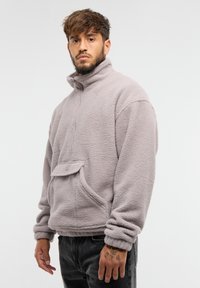 Polarowy pulower w jasnoszarym kolorze, z wysokim kołnierzem, półzamkiem, przednią kieszenią i ściągaczami przy mankietach, zaprojektowany dla ciepła i komfortu.