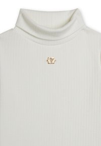Maglione a collo alto bianco a coste con una spilla dorata con design geometrico, tessuto strutturato e silhouette aderente.