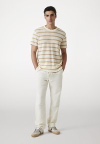 Gestreepte beige en crèmekleurige T-shirt gecombineerd met lichtbeige joggingbroek, met een relaxte pasvorm en een trekkoord in de taille. Afgemaakt met casual sneakers.