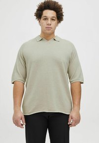 Polo shirt vert clair, texturé, à manches courtes avec col en V et col replié, associé à un pantalon noir.