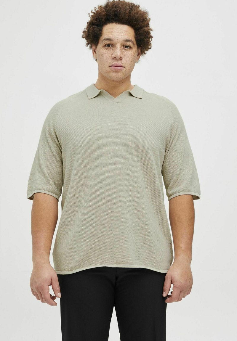 Polo shirt vert clair, texturé, à manches courtes avec col en V et col replié, associé à un pantalon noir.