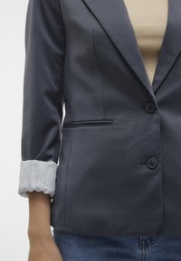 Námořnická sako s hladkou texturou, vybavené klopou, dvojitým zapínáním na knoflíky a manžetou s bílým detailem. Úzký střih s postranní kapsou.