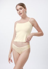 Camisole jaune avec bretelles fines, assortie à des culottes jaunes bordées de dentelle. Texture douce et lisse avec des détails en dentelle florale.