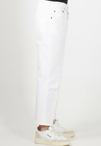 Pantaloni in denim bianco a gamba dritta con un classico design a cinque tasche, caratterizzati da accessori neri e una finitura pulita. Abbinati a sneakers bianche.