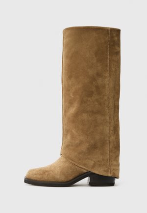 Braune Wildleder kniehohe Stiefel mit einer runden Spitze und einem niedrigen Absatz. Glatte Textur mit gesteppten Seitennähten und ohne sichtbare Beschläge.