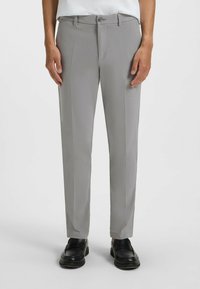 Pantaloni grigi su misura realizzati in tessuto morbido, con frontale piatto, passanti per cintura e chiusura con cerniera, abbinati a mocassini neri.