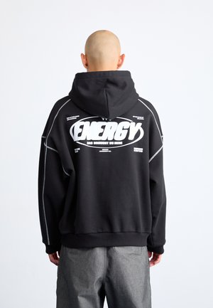 Black oversized hoodie with a drawstring hood, white graphic text on the back, ribbed cuffs, and contrasting stitching details.