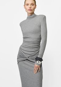 Hallidatud hall kleit pika varrukaga ja kõrge kaelusega. Omab kogutud tekstuuri ja keerduvat detaili vööl. Käes metallist randmeehtega.