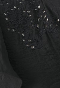 Czarna tkanina z misternym haftem kwiatowym i liściastym oraz wycięciami. Tekstura wydaje się gładka z delikatnym połyskiem.