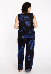 Ärmelloses Oberteil und weit geschnittene Hose aus schwarzem Stoff mit großen blauen Blumenmustern. Glatte Textur mit weichem Fall und lässiger Passform.