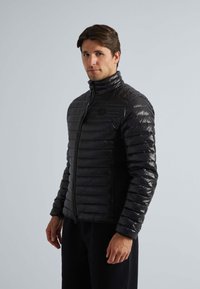 Zwarte puffjack met een horizontaal gestikt ontwerp, hoge kraag, ritsluiting en zijzakken. Gemaakt van glanzend, lichtgewicht materiaal.